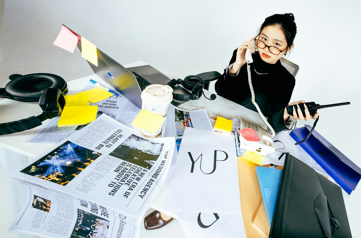 Người phụ nữ nói chuyện điện thoại tại bàn làm việc bừa bộn với giấy tờ